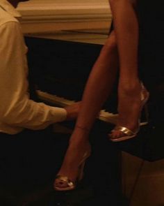 a woman in high heels sitting at a piano with her foot on the keyboard and another person standing next to her