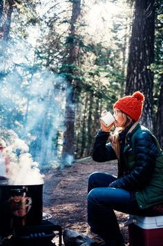 a person sitting at a campfire drinking from a mug