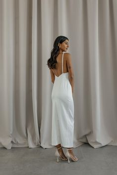 a woman standing in front of a curtain with her back to the camera and wearing a white dress