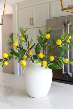 a white vase filled with yellow flowers on top of a counter