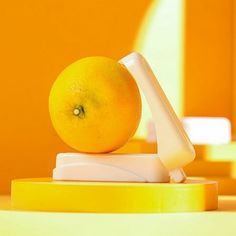 an orange sitting on top of a yellow stand with a white object in the middle