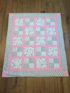 a pink and gray patchwork quilt laying on the floor next to a wooden floor