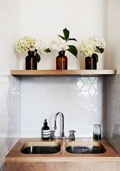 three vases with flowers sit on top of a shelf above a kitchen sink