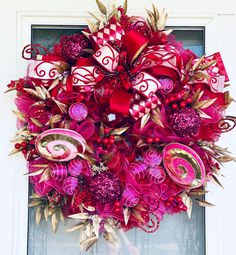 a wreath with red and pink decorations hanging on the front door to decorate it for christmas