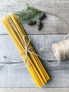 some yellow candles are tied up with twine and pine cones on the table next to them