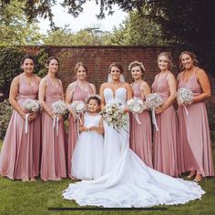 a group of women standing next to each other in front of a brick wall holding bouquets