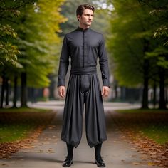 a man standing in the middle of a park wearing a long black outfit with pleated pants