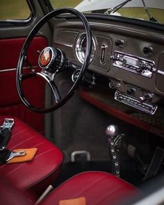 the interior of an old car with red leather seats and steering wheel, showing the dashboard