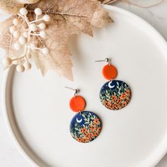 two orange and blue earrings sitting on top of a white plate