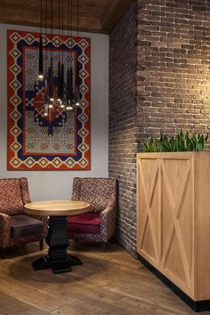 a room with two chairs, a table and a rug hanging on the brick wall