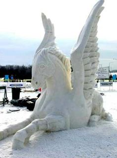 a white horse statue sitting in the snow with its wings spread out and it's eyes open