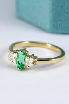 an emerald and diamond ring sitting on top of a white table next to a blue box