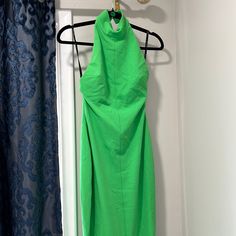 a green dress hanging on a hanger in front of a door with blue curtains