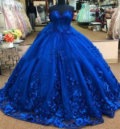 Embrace the magic of your quinceanera with this exquisite royal blue ball gown. The dramatic ball gown is crafted from luxurious tulle, and offers a voluminous, fairy-tale look, while the chapel train adds a regal flair, perfect for your grand entrance. The strapless neckline creates an elegant and timeless look, highlighting your shoulders and neckline with sophistication. What truly sets this gown apart are the stunning 3D flowers and applique detailing, which delicately adorn the bodice and s Floral Quince Dress, Royal Blue Princess Dress, Royal Blue Quince Dress, Floral Quince, Blue Quince Dress, Royal Blue Ball Gown, Ball Gown Sweet 16, Royal Blue Quinceanera Dresses, Royal Blue Quince