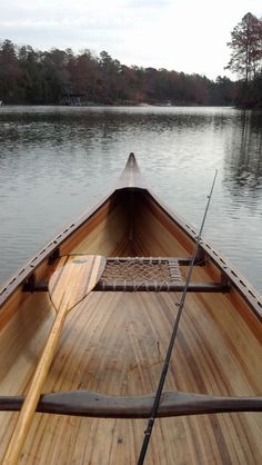 the front end of a wooden boat on a lake with trees in the back ground