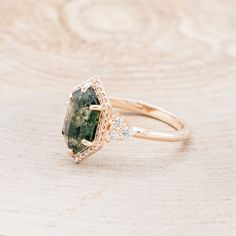 a close up of a ring with a green stone and diamonds on the side, sitting on a wooden surface