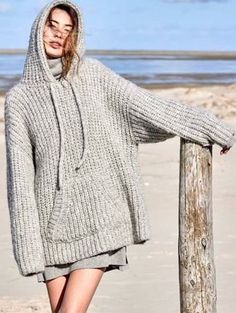 a woman is standing on the beach wearing a gray sweater and skirt with hoodie