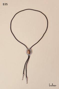 Tip your hat and up your aesthetic with the Petit Moments Western Wow Silver and Black Chunky Bolo Tie! This statement-making bolo tie has a woven faux leather cord with an adjustable, bolo-style toggle medallion at the front, which is composed of silver-toned metal and features an oversized, tiger's eye-like accent at the center. Matching embossed silver aglets complete the look. Adjustable bolo slide toggle. Necklace Measures 37" Long. 70% PU, 15% Zinc, 15% Quartz Stone. Imported. Lulus | West Bolo Tie Styling, Adjustable Brown Lariat Bolo Tie, Vintage Brown Bolo Tie With Adjustable Length, Adjustable Brown Western Jewelry, Vintage Adjustable Bolo Ties, Bohemian Brown Lariat Bolo Tie, Adjustable Brown Lariat Necklace, Brown Adjustable Lariat Necklace, Black Bohemian Lariat Necklace