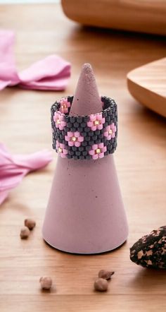 a purple cone with pink flowers on it sitting on a table next to some nuts