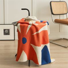 an orange and blue blanket sitting on top of a metal rack next to a chair