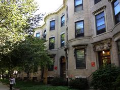 a person walking down a sidewalk in front of two buildings with trees and bushes on both sides