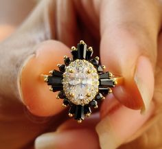 a close up of a person's hand holding an engagement ring with black and white stones