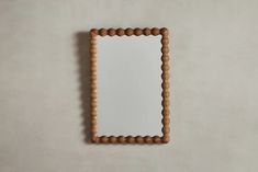 a mirror made out of wooden beads on the wall with a white background and light brown frame