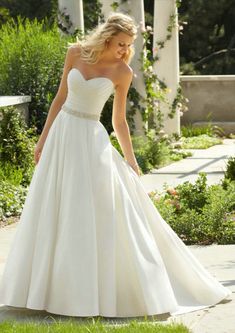 a woman in a white wedding dress is walking down the sidewalk with her hand on her hip