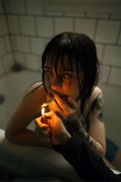 a woman sitting in a bathtub holding a lit candle up to her face and looking at the camera