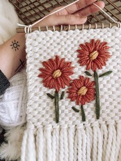 someone is holding up a piece of knitted art with red and yellow flowers on it