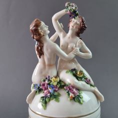 two figurines sitting on top of a white box with flowers around their necks