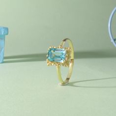 a gold ring with an aqua topazte surrounded by other jewelry items on a light green surface