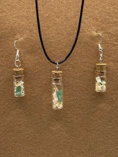 three glass bottles with flowers in them on a black cord necklace and earring set