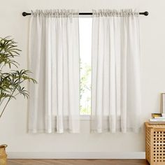 a white curtain hanging on the side of a window next to a potted plant