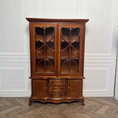 an old wooden china cabinet with glass doors on the top and bottom, against a white wall