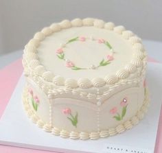 a decorated cake sitting on top of a white card board next to a pink table