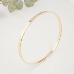 "Introducing our exquisite Solid 14K Gold Bangle, meticulously forged into a flawless round shape, this bangle epitomizes the artistry of skilled goldsmiths. Crafted from solid 14k gold, its solid construction ensures enduring beauty and resilience. Its robust 3mm width and 1.5mm thickness distinguishes it from more delicate alternatives. The lustrous surface reflects the unparalleled quality of the material, making it a luxurious addition to any jewelry collection. Each bangle will be made to order for you. Please enter your hand circumference. Bangle width: 3mm Bangle thickess: 1.5mm Bangle inside diameter: 6.5mm(2.5\") -measuring 19cm size" Modern 14k Gold Hoop Bracelets, Flexible Gold Cuff Bracelet, Flexible Yellow Gold Round Cuff Bracelet, Flexible Yellow Gold Cuff Bracelet, Minimalist 14k Gold Hoop Bangle, Timeless Gold Bangle Bracelet With Polished Finish, Modern 14k Gold Bangle Bracelet, Hoop Bracelet With Polished Finish As A Gift, Minimalist Polished Bangle