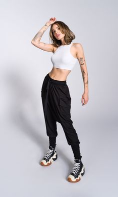 a woman in white top and black pants with tattoos on her arm posing for the camera