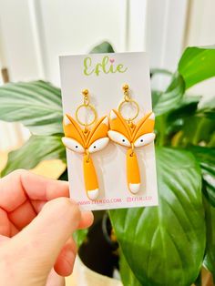 a pair of fox earrings is shown in front of a plant