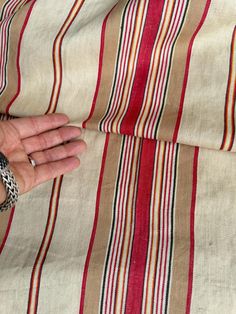 a person's hand on top of a red and beige striped fabric with stripes