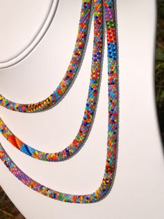 multicolored beaded necklaces are displayed on the back of a white toilet