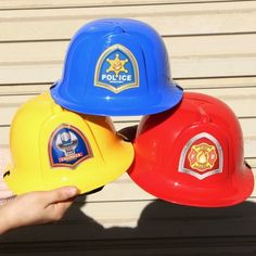 three children's hard hats with the words police written on them are held in front of each other