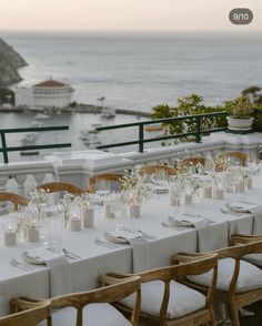 a long table with white linens and place settings is set for an outdoor dinner overlooking the ocean