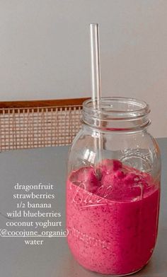 a jar filled with pink liquid sitting on top of a table next to a straw