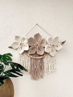 a white wall hanging with flowers on it next to a potted plant in a vase