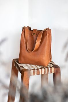 Natural-grained leather unlined tote featuring a top handle that can be hand-held or used on the shoulder. It comes with an adjustable and detachable strap. It has a central compartment with a zipper and is held shut by a sturdy snap closure. Brown Pebbled Leather Bag For Everyday, Brown Pebbled Leather Bag For Everyday Use, Everyday Leather Satchel With Top Handle, Everyday Bucket Bag With Detachable Double Handle, Everyday Leather Top Handle Satchel, Leather Satchel With Detachable Strap For Everyday, Leather Top Handle Satchel For Everyday, Travel Shoulder Bag With Textured Leather And Double Handles, Everyday Shoulder Bag With Detachable Double Handle