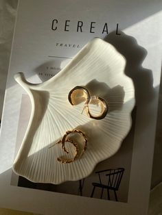 a book with two pairs of earrings on top of it next to a chair and table