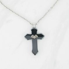 "Add a touch of traditional gothic style to your wardrobe with this cross pendant necklace. It would make a great addition to any dark jewelry collection! 💀 DESCRIPTION: This pendant necklace features a large cross made from hematite that was adorned with a small bat stamping. The cable chain was finished with a lobster clasp. 💀 SIZE & MATERIALS: The stamping was made from oxidized sterling silver plated brass. The chain was made from stainless steel and measures 18\" long. If you would li Traditional Goth, Dark Jewelry, Hematite Stone, Goth Jewelry, Wing Necklace, Black Chain, Halloween Accessories, Cross Pendant Necklace, Oxidized Sterling Silver