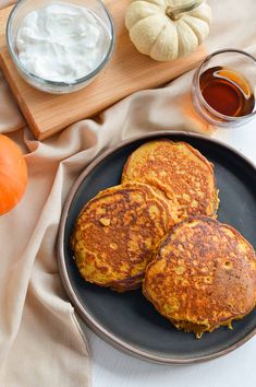 three pancakes on a black plate with butter and pumpkins in the background, along with two glasses of orange juice