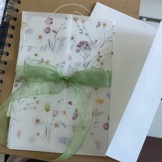 a notepad with a green ribbon tied to it next to a spiral bound notebook